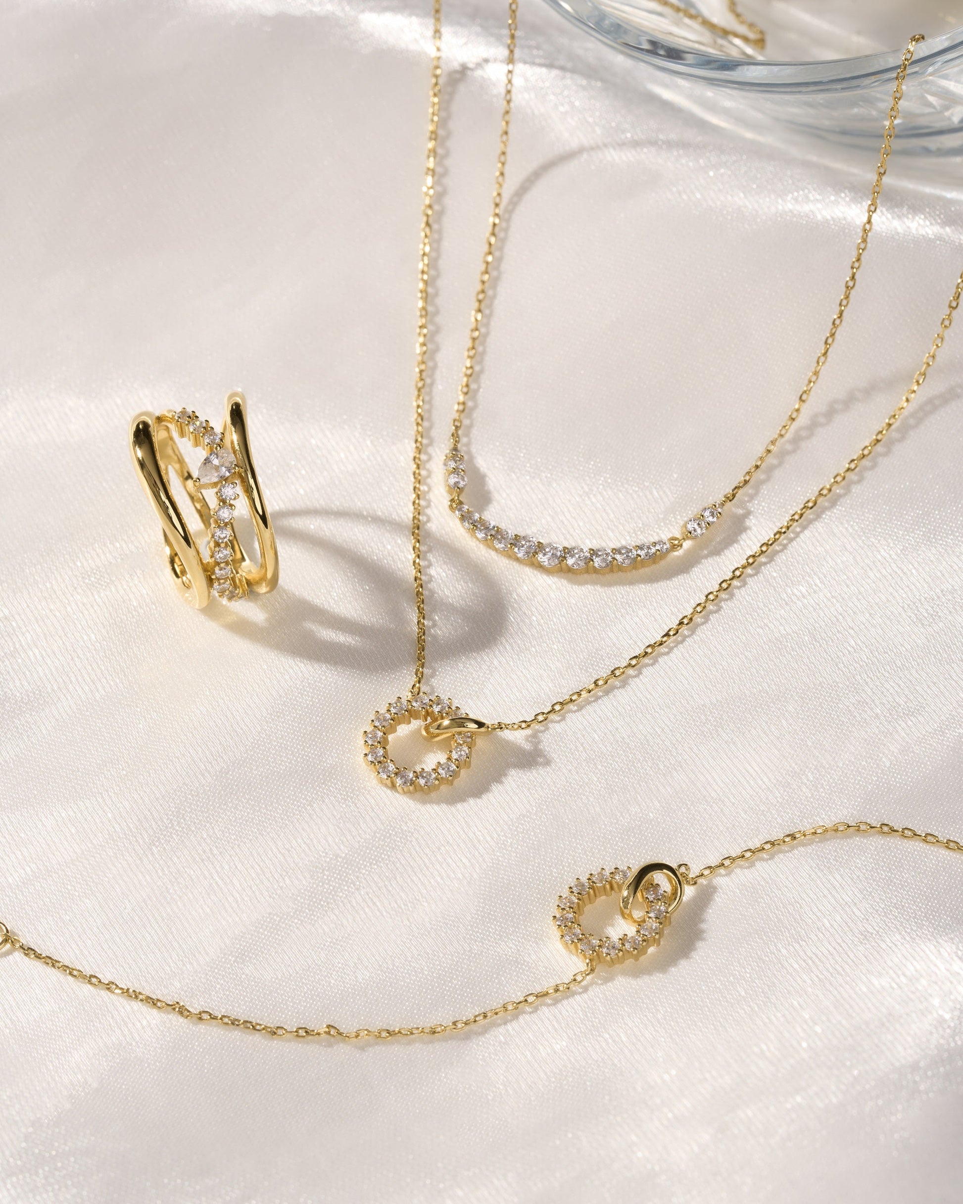 Gold interlinked circles pavé necklace with matching bracelet and ring on white silk